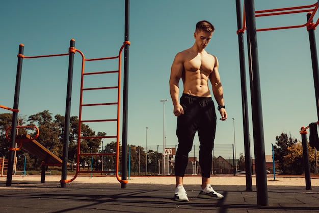 Man met een mooi atletisch lichaam poseert terwijl hij naast de horizontale balken staat