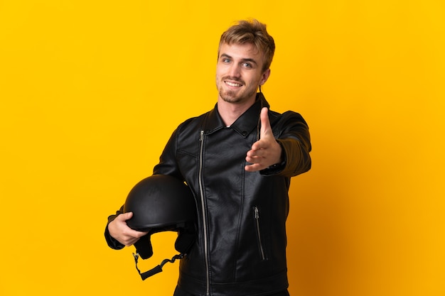 Man met een motorhelm geïsoleerd op geel handen schudden voor het sluiten van een goede deal