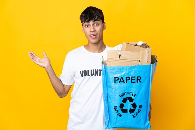 Man met een recyclingzak vol papier om te recyclen over geïsoleerde gele muur met geschokte gezichtsuitdrukking