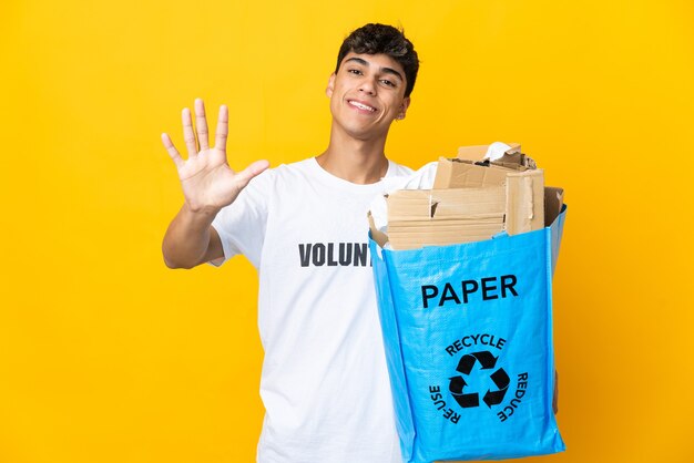 Man met een recyclingzak vol papier om te recyclen over geïsoleerde gele muur vijf tellen met vingers