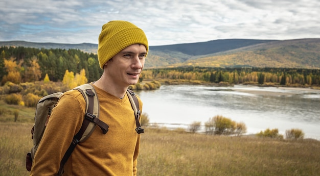 Man met een rugzak loopt langs rivier, gouden bos en heuvels. Concept van vrijheid, reizen, wandelen en herfststemming