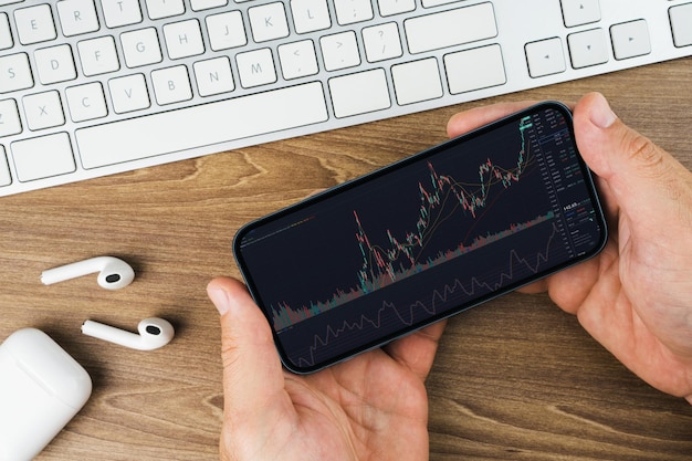 Man met een smartphone met financiële beurs grafiek op het scherm op houten achtergrond tafel Kantooromgeving Stock Exchange