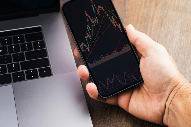 Man met een smartphone met financiële beursgrafiek op de houten tafel Kantooromgeving Stock Exchange