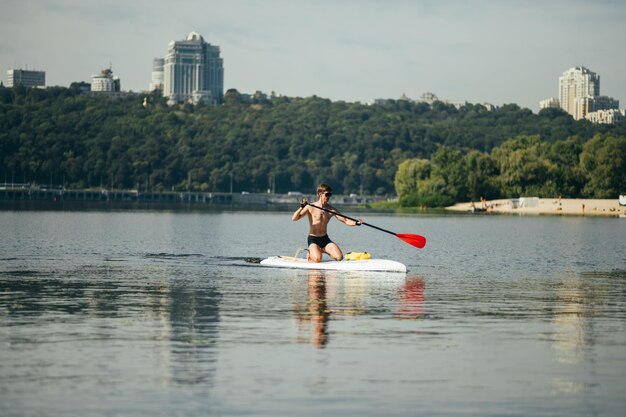 man met een sportief lichaam peddelt op een sup board op de rivier op de achtergrond van een prachtig landschap