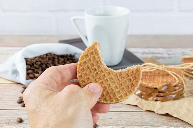 Man met een stroopwafel met een hapje. Op de achtergrond bonen en kopje koffie.