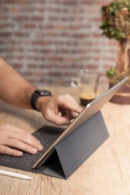 Man met een tabletcomputer om te werken, op een houten tafel met een kopje koffie, voor een bakstenen muur