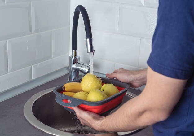 Foto man met een vergiet met fruit onder stromend water in de keuken fruit wassen