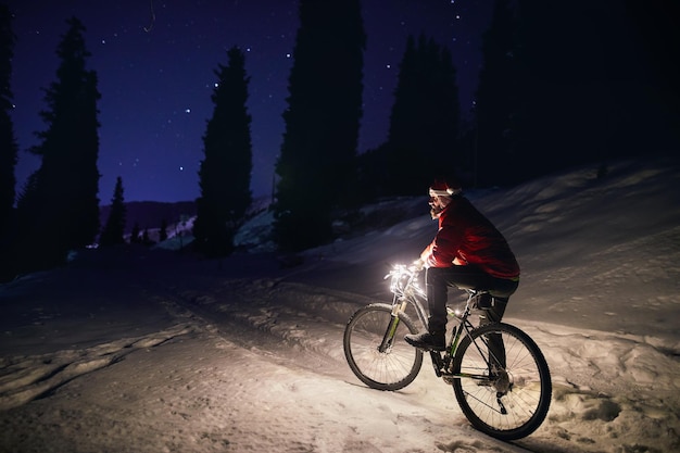 Man met fiets in het winterbos 's nachts