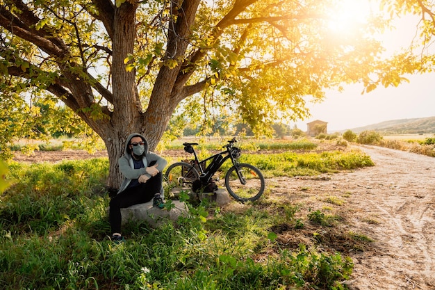 Foto man met fiets zit bij boom op het veld tegen de lucht