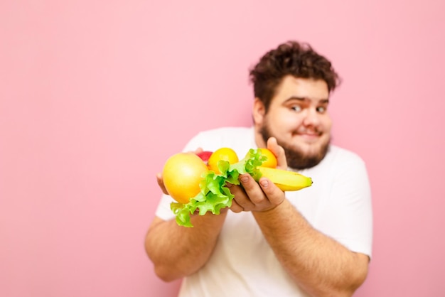 man met fruit in handen geïsoleerd op roze achtergrond Fruit en groen in de handen van een dikke man