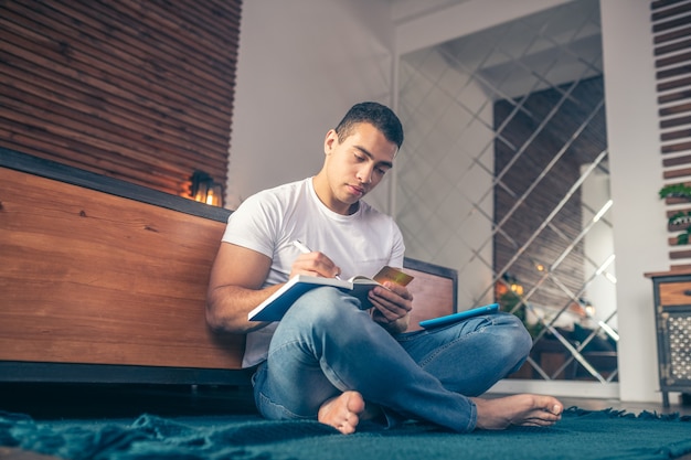 Man met gekruiste benen met creditcard die in notitieboekje schrijft.