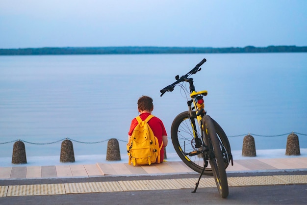 Man met gele rugzak zit alleen aan het meer in de stad Reizen met de fiets