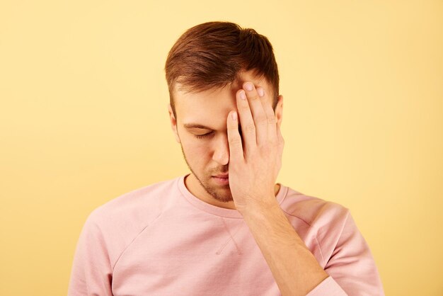 Man met gesloten ogen bedekt de helft van zijn gezicht met hand op gele achtergrond geïsoleerd concept van hoofdpijn schuldgevoel en frustratie