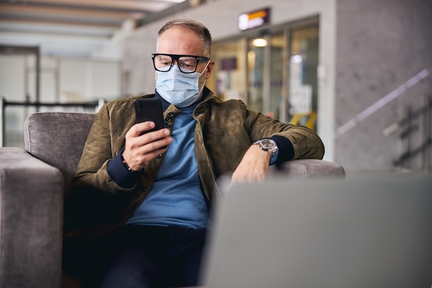 Man met gezichtsmasker staart naar zijn gadget