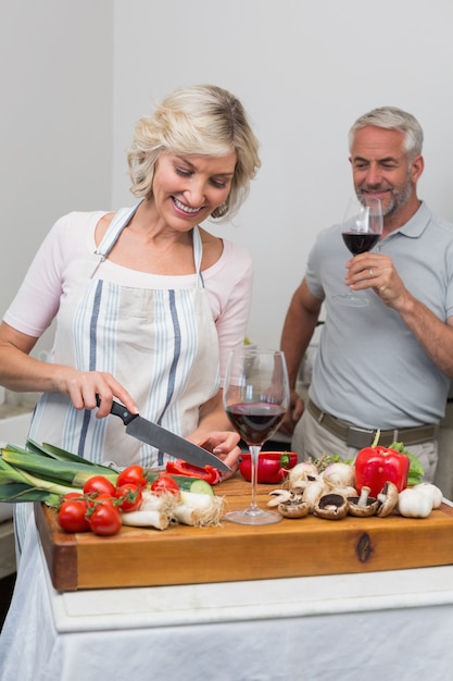 Man met glas wijn en vrouw hakken groenten in de keuken