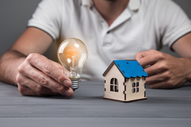 Man met gloeilamp en huis op grijze muur