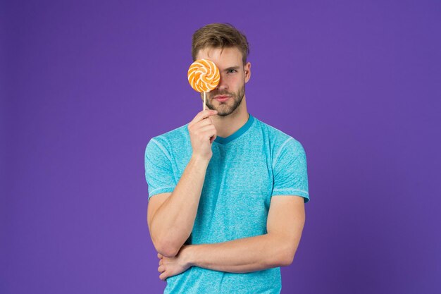 Man met haren houdt van lolly Cheat maaltijd concept Suiker schadelijk voor de gezondheid Guy hold lolly snoep violette achtergrond Smaak van de kindertijd Lollipop plezier Man eet grote kleurrijke zoete lolly