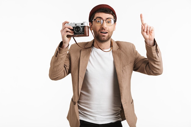 man met hipster hoed die zich verheugt terwijl hij vasthoudt en fotografeert op retro voorkant geïsoleerd over witte muur