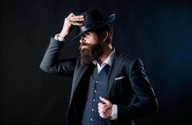 Man met hoed Vintage mode Man goed verzorgde bebaarde heer op donkere achtergrond Mannenmode en herenkleding Retro mode hoed Formeel pak klassieke stijl outfit Elegante en stijlvolle hipster