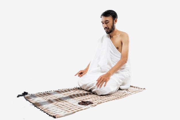 Man met ihram biddend met gebedskleed terwijl hij zit tasyahud