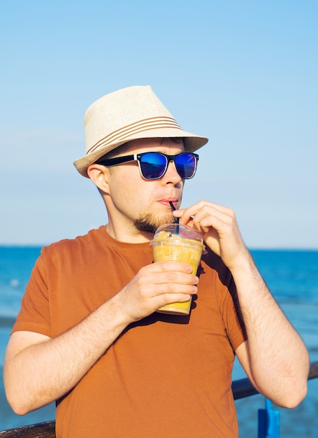 Man met koffie frappe in de buurt van zee die zich vrij voelt en geniet van vrije tijdvakanties.