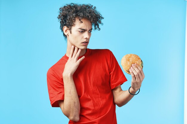 Man met krullend haar in rode t-shirt hamburger fastfood blauwe achtergrond Hoge kwaliteit foto