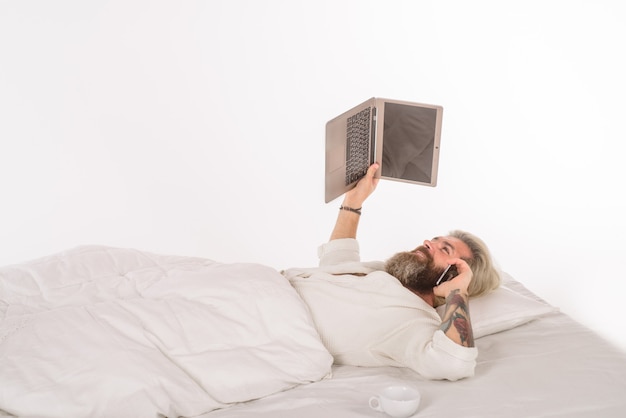 Man met laptop aan het werk in bed zelfisolatie werk vanuit huis man met laptop en smartphone