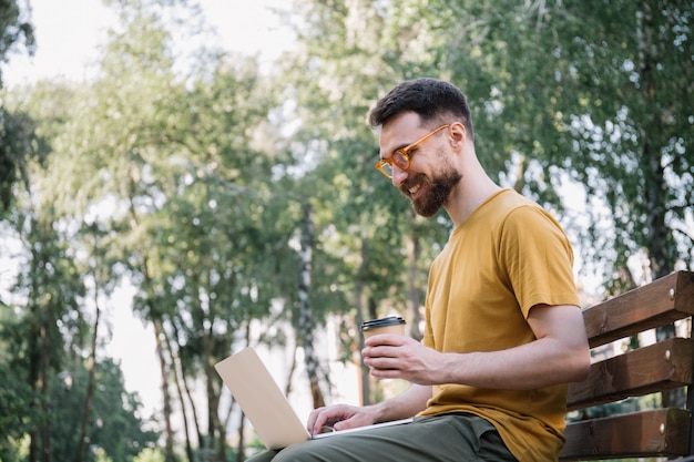 Man met laptop, kopje koffie, zittend op de bank te houden. Freelancer copywriter werken in park