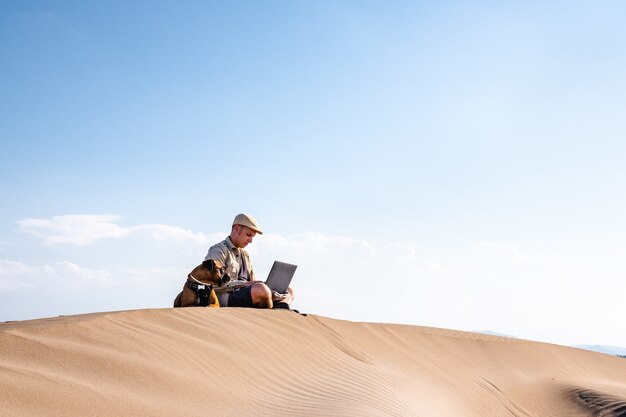 Man met laptop met hond op zandduin in de zomer