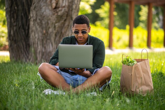 Man met laptop zittend op gras in park