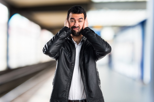 Man met lederen jas die zijn oren op ongerichte achtergrond bedekt