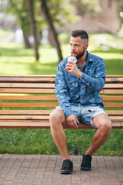 man met limonade rust in een park op een bankje in het voorjaar. Zonnige dag.