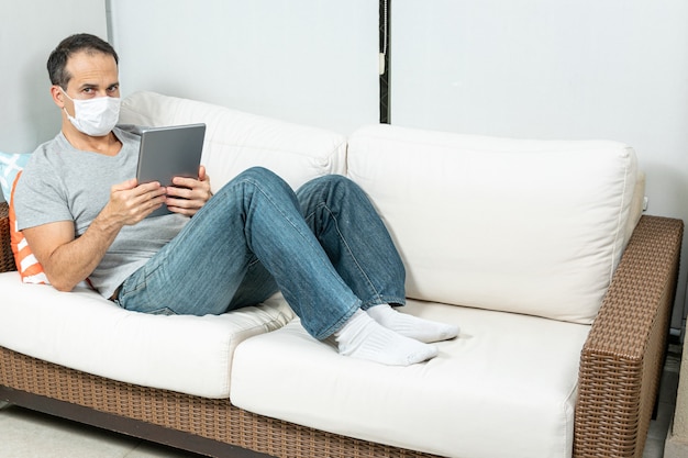 man met masker kijken naar de tablet op de bank