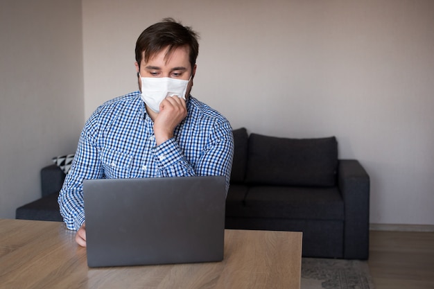 Man met masker werken op zijn laptop vanuit huis, coronavirus, ziekte, infectie, quarantaine, medisch masker