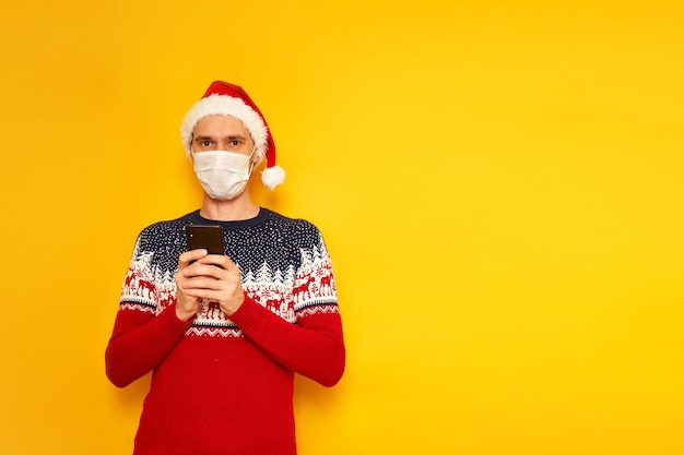 man met medisch masker Kersttrui Kerstmuts houdt smartphone in zijn handen schrijft bericht