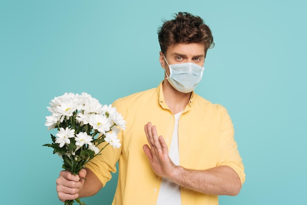 Man met medisch masker met uitgestrekt handboeket en geen teken geïsoleerd op blauw