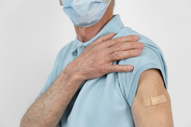 Foto man met medisch masker met verband op arm na vaccinatie