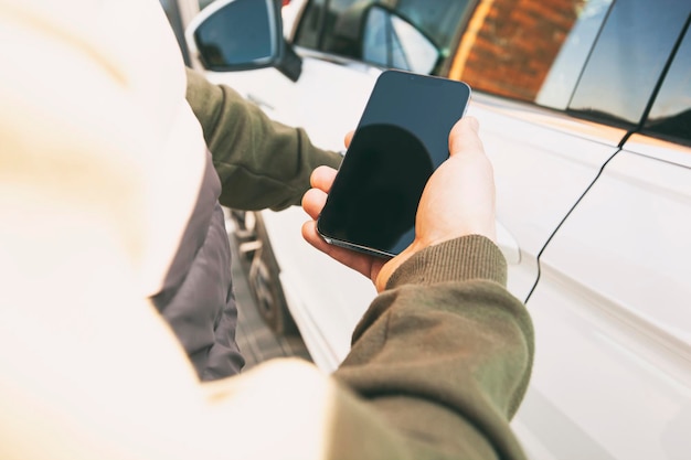 Man met mobiele telefoon naast de deur van zijn auto op straat