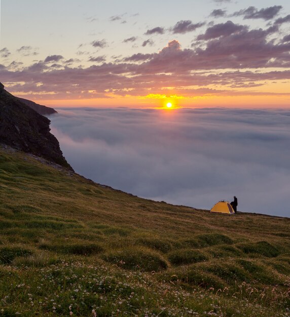 Man met oranje tent bij zonsondergang op de rotsen van het eiland Soroya, Noorwegen