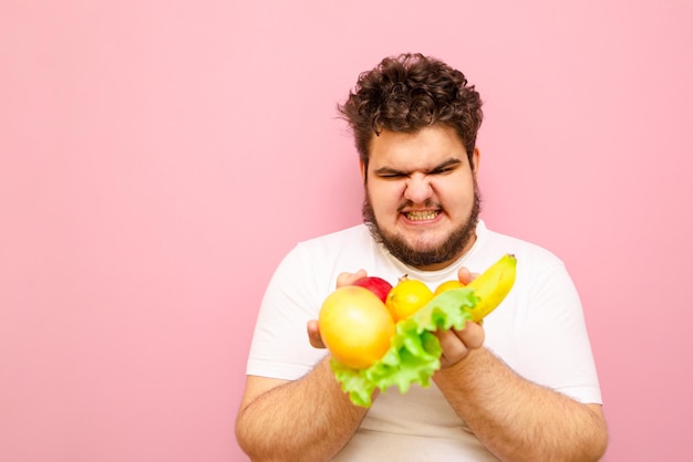 Man met overgewicht is niet blij met zijn dieet houdt fruit en sla in zijn handen