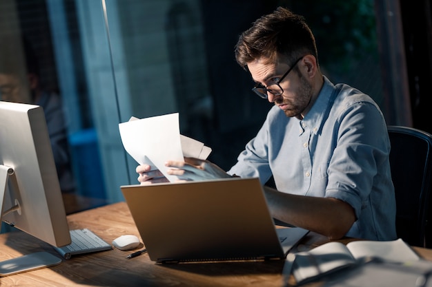 Man met papieren op laptop