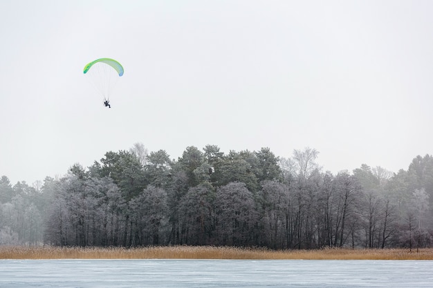 Man met parachute-paragliding hoog in de lucht boven rijpbomen en bevroren meer