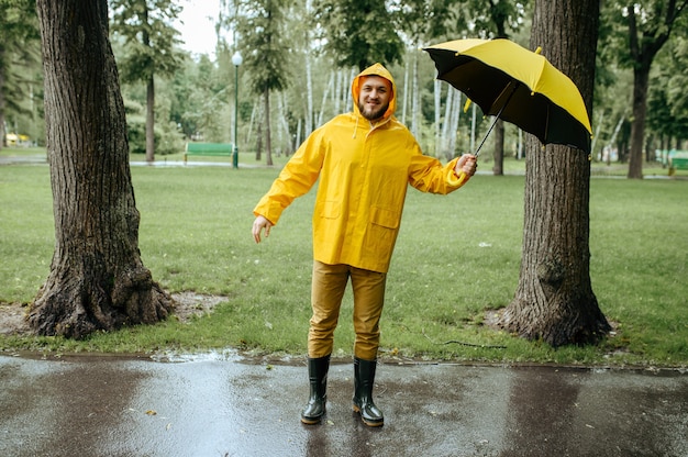 Foto man met paraplu wandelen in zomer park in winderige regenachtige dag. mannelijke persoon in regenkaap en rubberen laarzen, nat weer in steegje