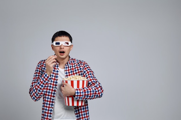 Foto man met rood-blauwe 3d-bril en het eten van popcorn uit de emmer tijdens het kijken naar een film geïsoleerd op grijs