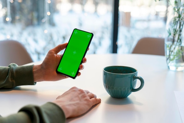 Man met smartphone met Chroma Key-scherm in café aan witte tafel koffie drinken groen scherm man's handen zakelijke mock up