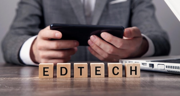 Man met smartphone met een woord EdTech op houten kubussen.
