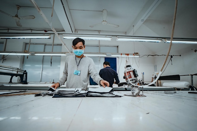 Man met snijmachine en persoonlijke beschermingsmiddelen op industriële kledingwerkplaats Stoffensnijder in Aziatische textielkledingfabriek