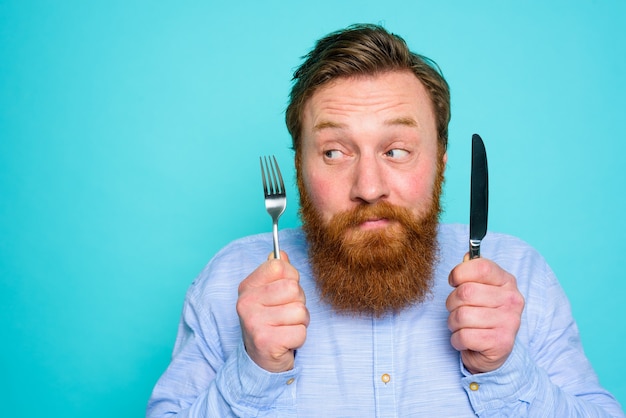 Man met tatoeages is klaar om te eten met bestek in de hand