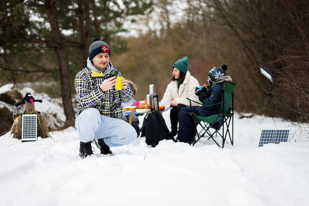 Man met telefoon bij de hand tegen zijn familie in het winterbos samen tijd doorbrengen op een picknick