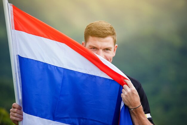 Foto man met thaise vlag staat op het veld tegenover bergen